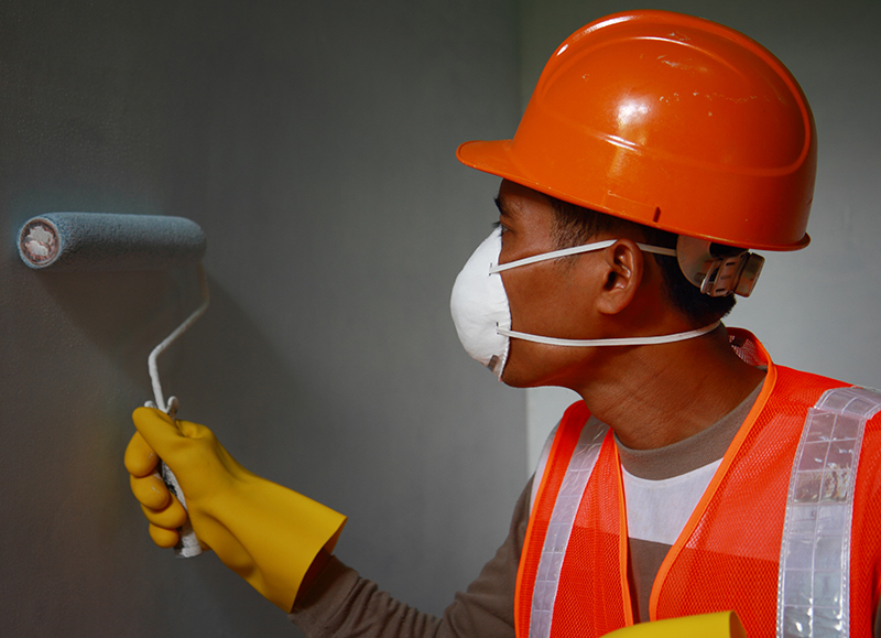 Painter worker wearing safety mask or safety work on job, painting of building house or apartment wall with roll